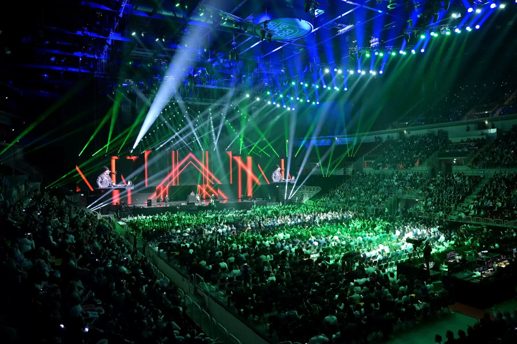 Showbühne mit grünen und weißen Lichtstrahlen über einer ausverkauften Halle