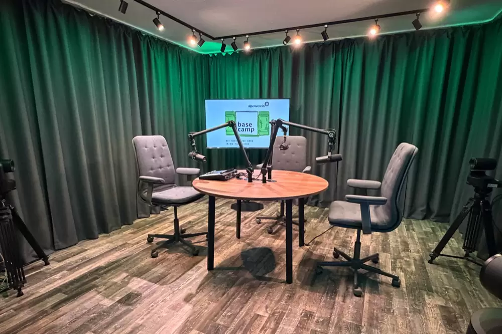 Podcaststudio von Basecamp mit rundem Tisch, Mikrofonen und grünem Vorhang