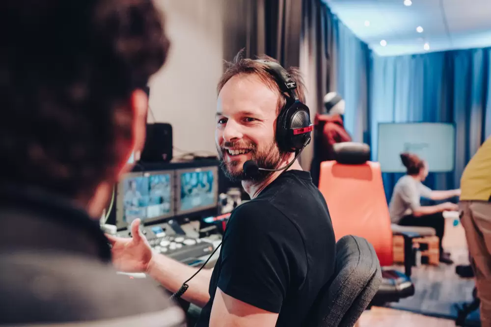 Florian Rudig mit Headset am Regiepult, umgeben von Monitoren