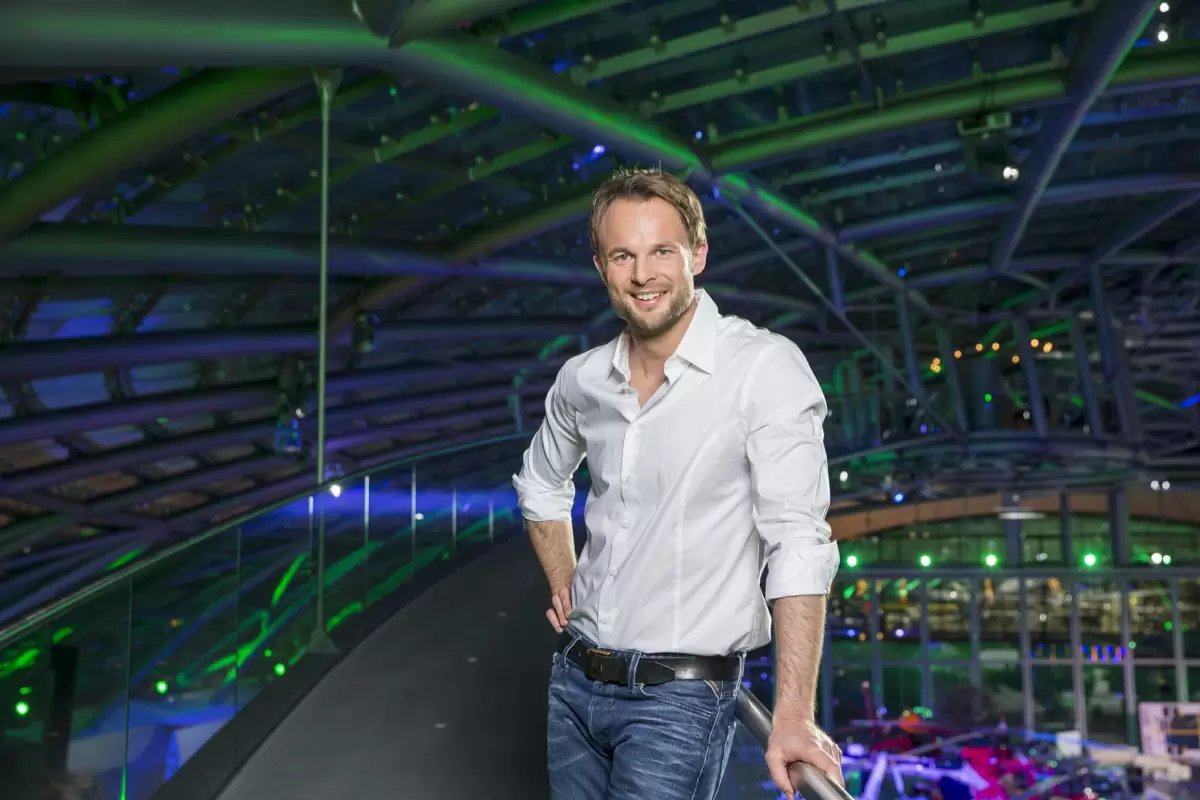 Florian Rudig steht im weißen Hemd auf dem Set im Hangar-7, hinter ihm die grün beleuchtete Glaskuppel und Flugzeuge Florian Rudig steht im weißen Hemd auf dem Set im Hangar-7, hinter ihm die grün beleuchtete Glaskuppel und Flugzeuge